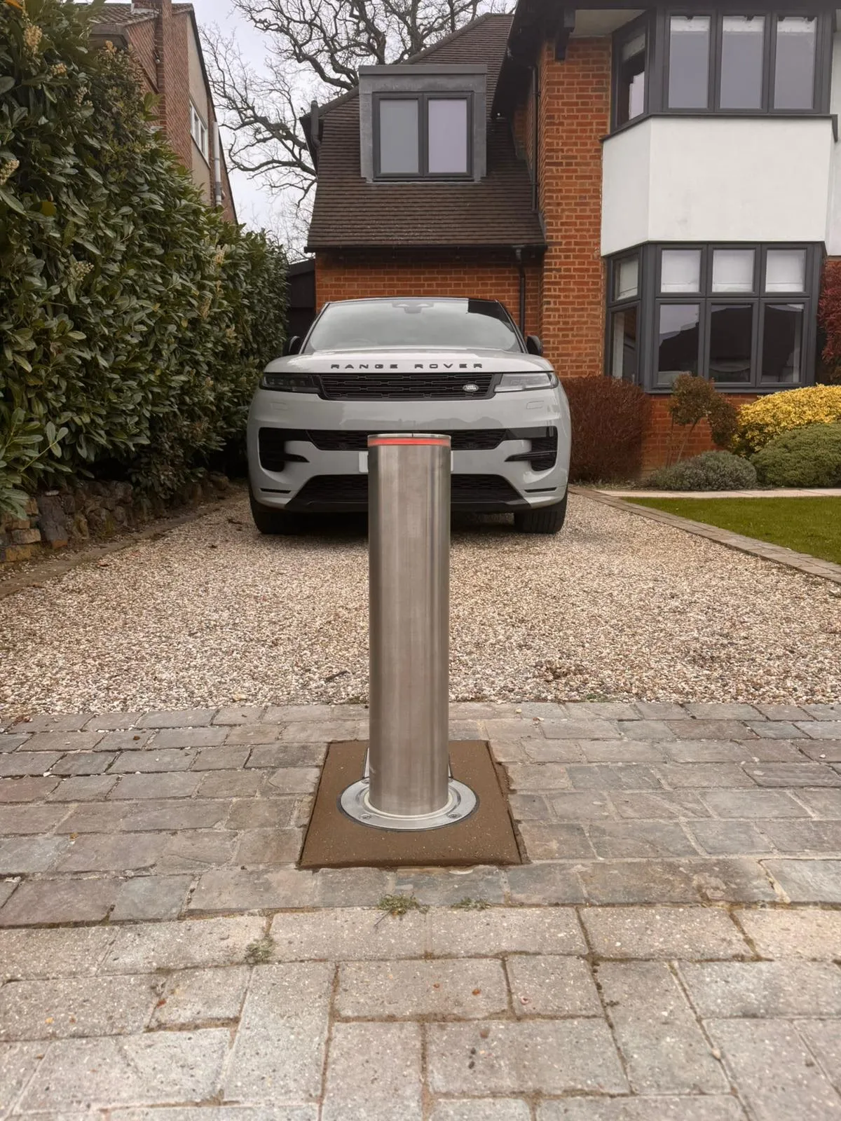 Stainless steel automatic security bollard raised in front of a Range Rover on a block-paved driveway